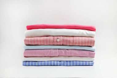 Renkli, mükemmel katlanmış giysi yığını. Farklı pastel renkli gömlek yığınları, izole edilmiş süveterler ve beyaz arka planda başka giysiler. Kapat, boşluğu kopyala.