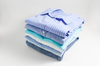 Renkli, mükemmel katlanmış giysi yığını. Farklı pastel renkli gömlek yığınları, izole edilmiş süveterler ve beyaz arka planda başka giysiler. Kapat, üst görünüm, boşluğu kopyala.