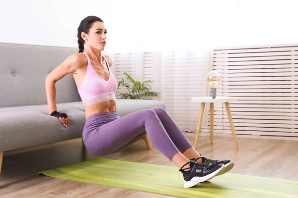 Evde çalışma konseptinde kal. Genç ve çekici bir kadın dairesinde vücut ağırlığı egzersizleri yapıyor. Güzel bir kadın kanepe kullanarak triseptik dalış yapıyor. Kapat, kopyala boşluk, arkaplan.