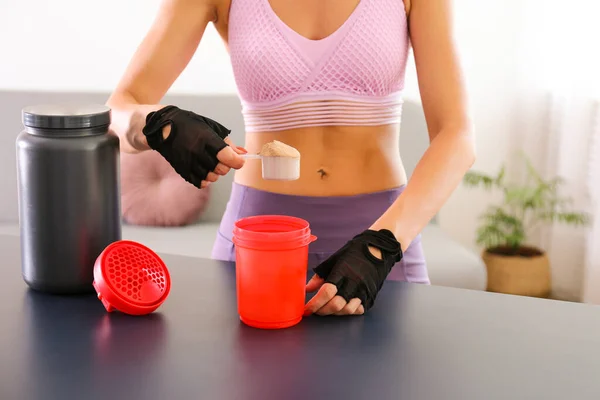 Evde eğitim konseptinde kal. Sportif vücutlu çekici bir kadın egzersiz sonrası protein içeceği içiyor. Kadın spor kıyafetleri içinde güzel bir kadın elinde kırmızı bir tokalaşma aleti tutuyor. Kapat, arkaplanı kopyala