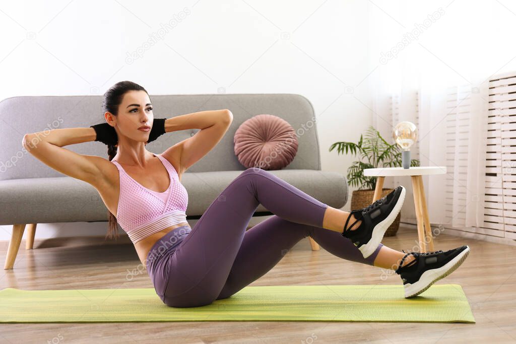 Stay at home workout concept. Young attractive female performing bodyweight fitness exercises at her apartment. Beautiful female training abs, doing sit ups. Close up, copy space, background.