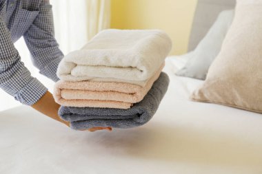 Hizmetçi kadın otel odasındaki katlanmış ve istiflenmiş havluları değiştiriyor. Temiz ve ütülenmiş çarşaflar güneş ışığında. Kapat, metin için boşluk kopyala.