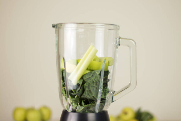 Blender jar with green leaves, celery and apples. Fruits and veg
