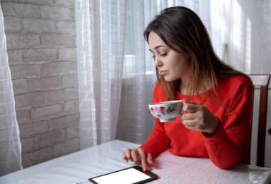 Mutfaktaki masada dijital kitap okuyan bir kız.