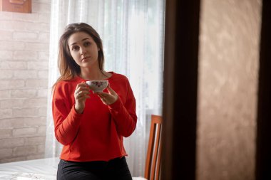 Mutfaktaki masada elinde fincanla duran bir kız.