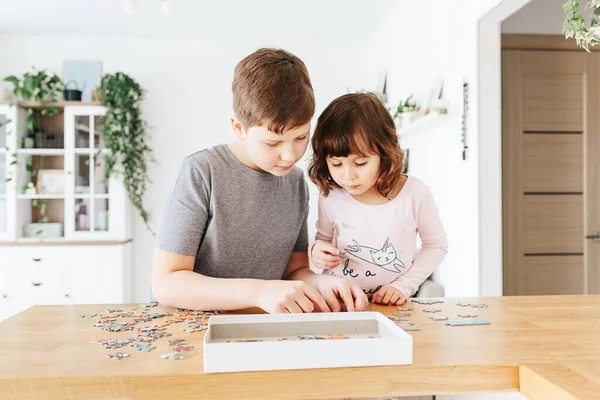 Brother and sister playing puzzles at home. Children connecting jigsaw puzzle pieces in a living room table. Kids assembling a jigsaw puzzle. Fun family leisure. Stay at home activity for kids.