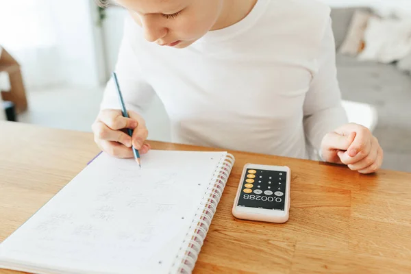 Hard-working school kid boy making homework math using calculator writing note with pencil. Education and distance learning for kids. Homeschooling during quarantine. Homeschooling concept