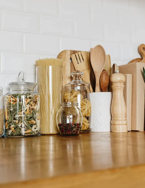 Various pasta types in glass jars on the wooden table in the kitchen. Kitchen interior ideas. Eco friendly kitchen, zero waste home concept