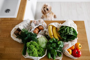 Fresh vegetables and fruits in eco cotton reusable bags on table in the kitchen. zero waste shopping concept. Sustainable living clipart