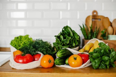 Taze sebzeler ve meyveler eko pamukta yeniden kullanılabilir poşetler mutfakta ahşap masada. sıfır atık alışveriş konsepti. Sürdürülebilir yaşam