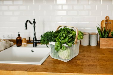 Mutfaktaki masada metal sepetin içinde taze salatalar ve otlar. sıfır atık alışveriş konsepti. Sürdürülebilir yaşam