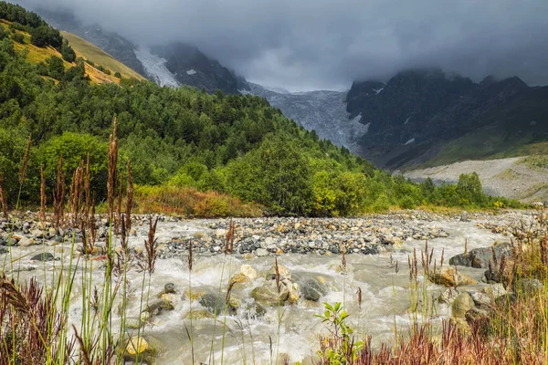 Rio rochoso de montanha forte Adishchala e a sua geleira de fonte Lardaad em um contexto na luz sombria — Fotografia de Stock