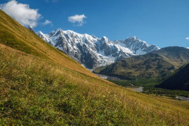 Mavi açık gökyüzü güneşli bir gün. Kar yeşil yamaçlı büyük dağlar. Otlarla kaplı Svaneti Georgia.