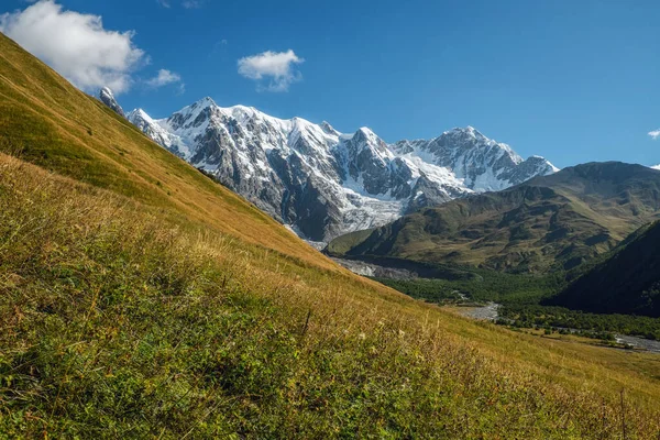 Cielo azul claro día soleado grandes montañas con nieve pendiente verde con hierba Svaneti Georgia — Foto de Stock