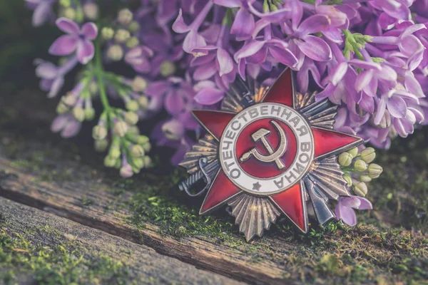 The Soviet order with Russian words Great Patriotic War, natural moss background with lilac branch, Victory Day 9 May