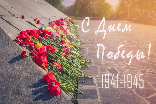With Victory day 1941-1945 - Russian text. Tulips and carnation flowers at the military monument in memory of Second World War, May 9 holiday greeting postcard