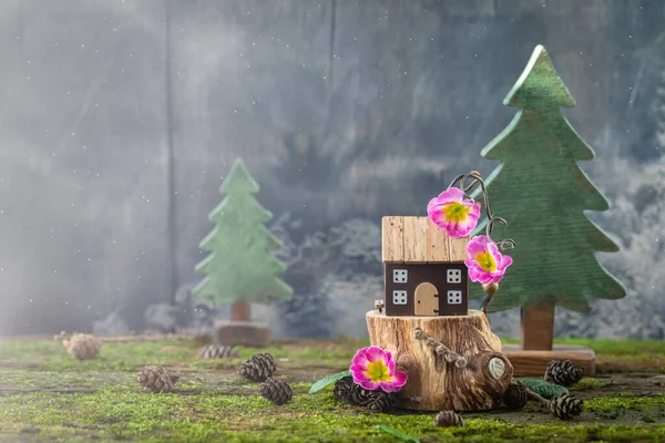 Miniature wooden toy house cottage with pink flowers on moss background, spring Easter, Earth Day postcard concept, copyspace
