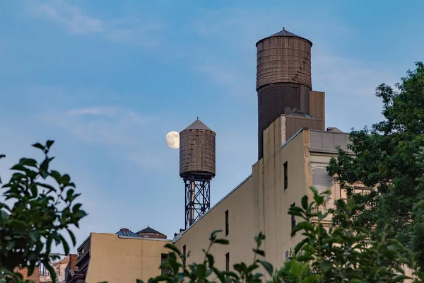 Full moon rising behind water tower on the roof of buildings in — Stock Photo, Image