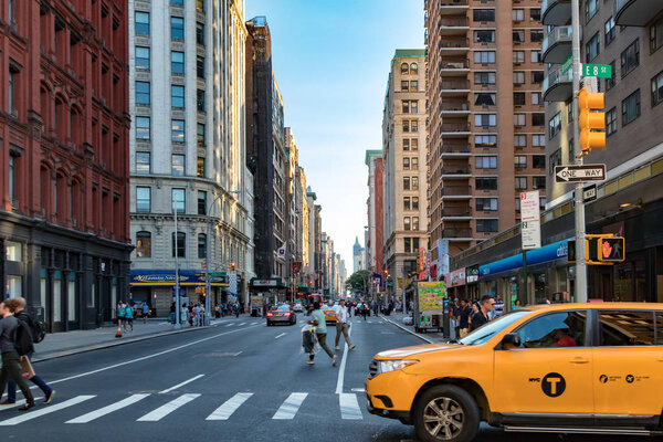 NEW YORK CITY - CIRCA 2017: Yellow taxi cab turning onto Broadway with people crossing the 8th Street intersection in Manhattan, New York City.