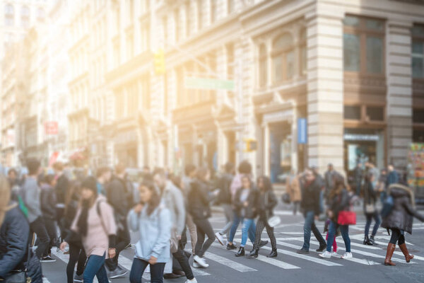 Anonymous people crossing street in SoHo New York City with sunlight in background