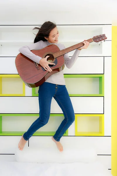 Asian girl with guitar jump in bedroom