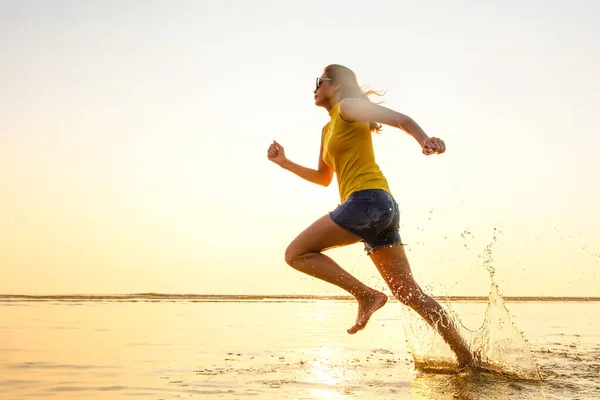 在阳光下 赤脚女子在浅水区的海滩上慢跑 空气中的水滴随着动力运动而结冰 采用高速快门速度技术拍摄 — 图库照片