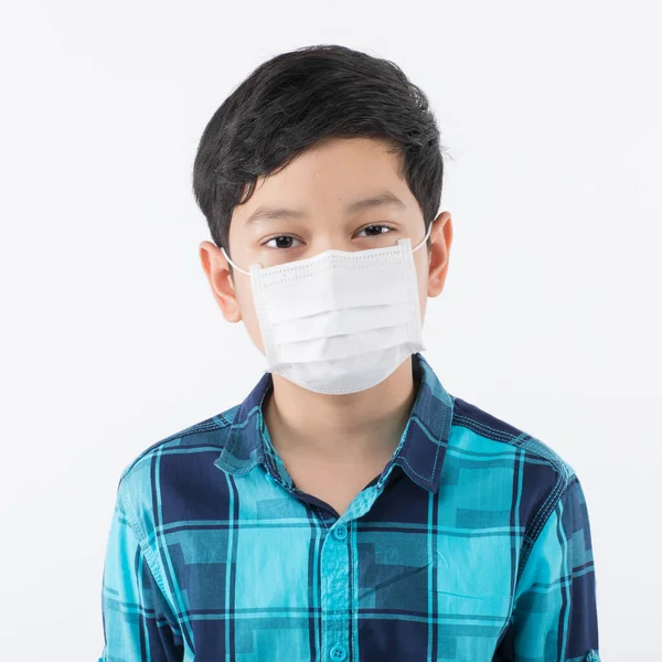 白い背景に外科用保護マスクをした幼いアサン少年がカメラを見ている 健康管理と子供がコロナウイルスの発生や汚れた大気汚染のリスクを防ぐためのアイデア — ストック写真