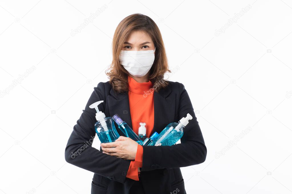 Beautiful Asian woman in suit business dress on white background wearing surgical protect mask and holding many sizes of hand wash alcohol gel bottles in hands. Concep for preparing to prevent virus.