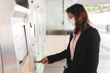 Siyah takım elbiseli, tıbbi hijyen koruyucu maske takan güzel bir Asyalı kadın istasyonda metro ya da gökyüzü tren otomatı alıyor. İşçi konsepti, sağlığın koronavirüs veya covid-19 'dan korunmasını önler