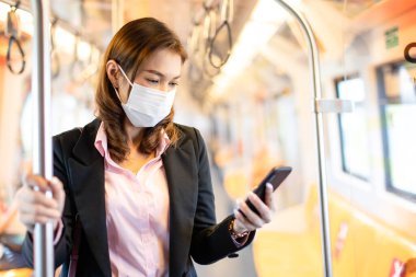 Tıbbî hijyen maskesi takan eğitimli Asyalı iş kadını yolcu. Metroda ya da trenle gidip gelirken cep telefonu kullanmak. Coronavirüs salgını fikri ile çalışma tarzı