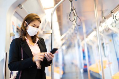 Tıbbî hijyen maskesi takan, çalışkan, Asyalı bir iş kadını yolcu. Boş metro ya da gökyüzü vagonunda cep telefonu kullanmak. Terk edilmiş şehir için COVID-19 'dan fikir.
