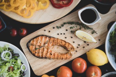 Tahta tabakta dilimlenmiş lezzetli somon bifteği, çeşitli taze sebzeler, limon, domates ve salata kasesi, Omega 3 yağ ve beslenme gerçeği bakımından zengindir. Sağlıklı ve diyet yiyecekler üst açı.