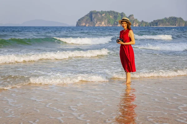 Kırmızı Elbiseli Kadın Fotoğrafçı Sahilde Suya Batmış Kamerayı Elinde Tutuyor — Stok fotoğraf