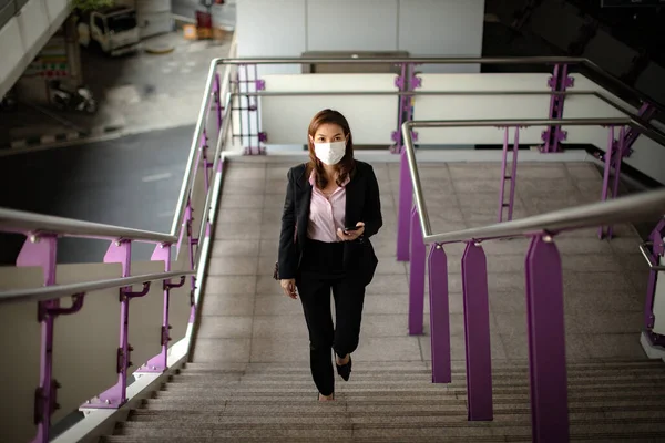 身穿黑色西服 戴着医疗卫生防护面具的美丽的亚洲女人走在城市的楼梯上上班 关于保健和预防大肠病毒流行病爆发风险的构想 — 图库照片