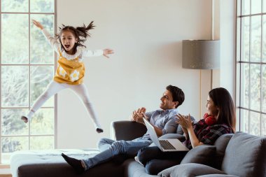 Üç farklı aile üyesi, beyaz bir baba, Asyalı bir anne ve küçük bir üvey kız birlikte oturma odasında vakit geçiriyorlar. Annem ve babam evde çalışırken kız kanepede zıplayıp neşeleniyor..