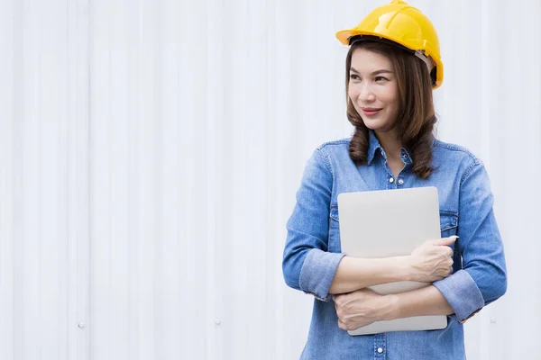 Schöne Asiatische Ingenieurin Jeans Trägt Einen Gelben Schutzhelm Mit Laptop lizenzfreie Stockbilder