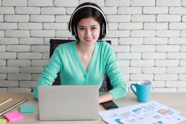 Genç, güzel ve yarı güzel Taylandlı kız ders odasında grafik ve çizelge kağıdıyla çalışırken masabaşı gibi oturup gülümsüyor. Evden çalışma fikri.