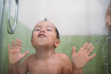 Çocuk duş kabininde ve cama yaslanıyor.