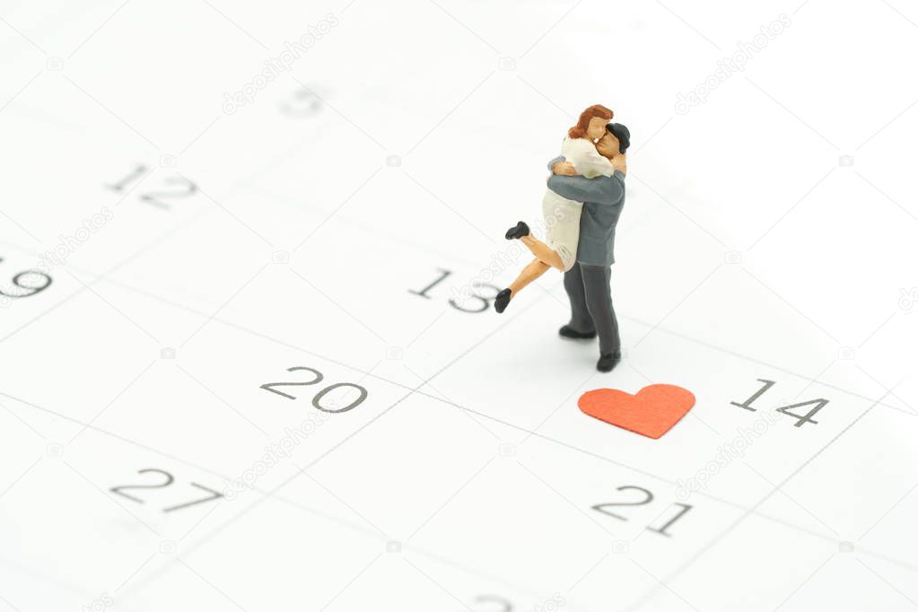 Couple Miniature 2 people standing on Calendar. Day 14 meets Valentine Day with Heart shaped red paper. Red heart is the promise of love. using as background Valentine concept with copy spaces for you