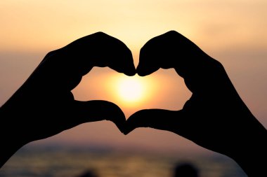 Kalp şeklinde siluet eliyle gündoğumu kavramında orta ve plaj olarak arka plan Sevgililer kopya boşluklu metin veya tasarım için.