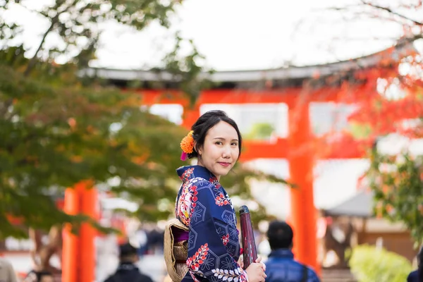 Geishas girl wearing Japanese kimono among red wooden Tori Gate