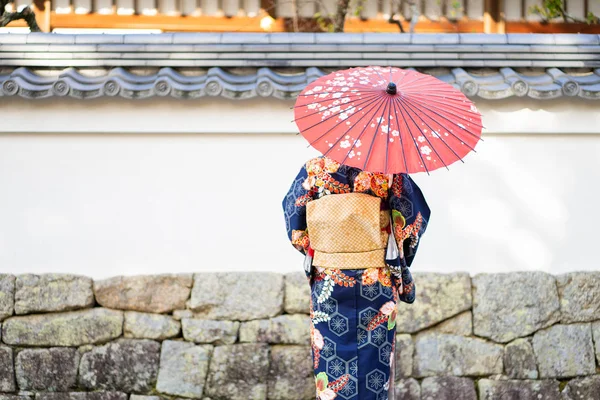 Geishas girl wearing Japanese kimono among red wooden Tori Gate at Fushimi Inari Shrine in Kyoto, Kimono is a Japanese traditional garment. The word \