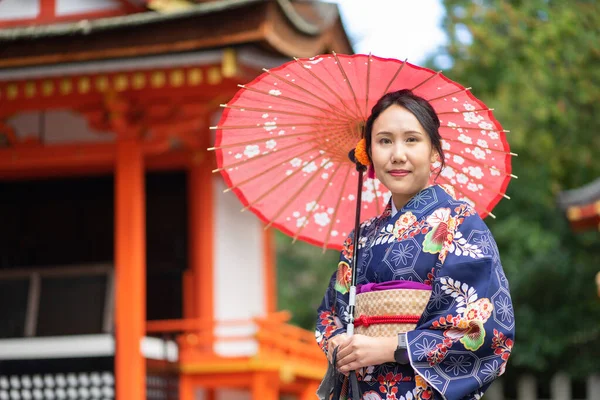 京都の伏見稲荷神社にある赤い木製の鳥居の中に日本の着物を着た芸者の女の子 着物は日本の伝統的な服です 着物という言葉は 実際には 着るもの を意味します — ストック写真