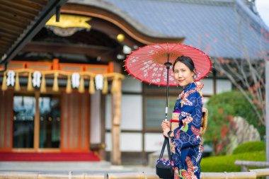 Geishas girl wearing Japanese kimono among red wooden Tori Gate at Fushimi Inari Shrine in Kyoto, Kimono is a Japanese traditional garment. The word 