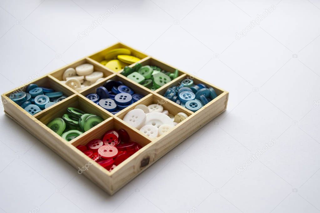 Clothes buttons in wooden box on white cardboard background. Clo