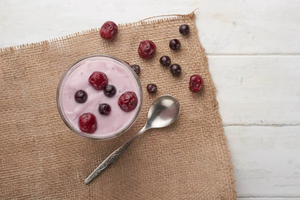 yogurt in a glass with berries on sacking and texture