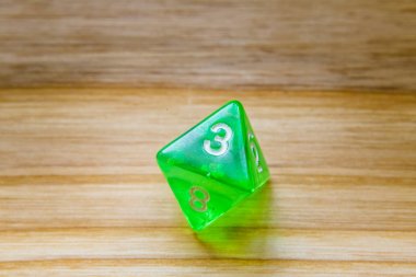 A translucent green eight sided playing dice on a wooden backgro clipart