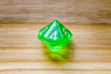 A translucent green ten sided playing dice on a wooden backgroun clipart