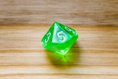 A translucent green ten sided playing dice on a wooden backgroun clipart
