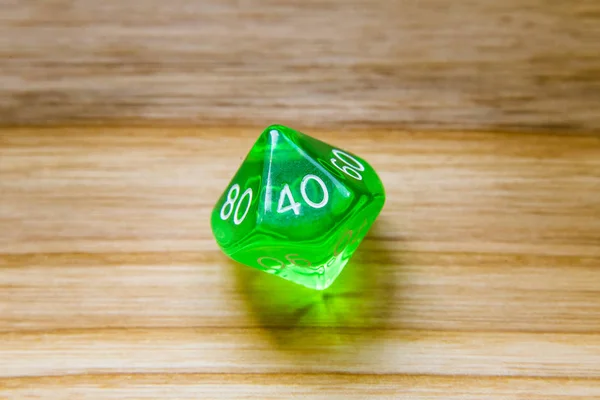 A translucent green ten sided playing dice on a wooden backgroun — Stock Photo, Image